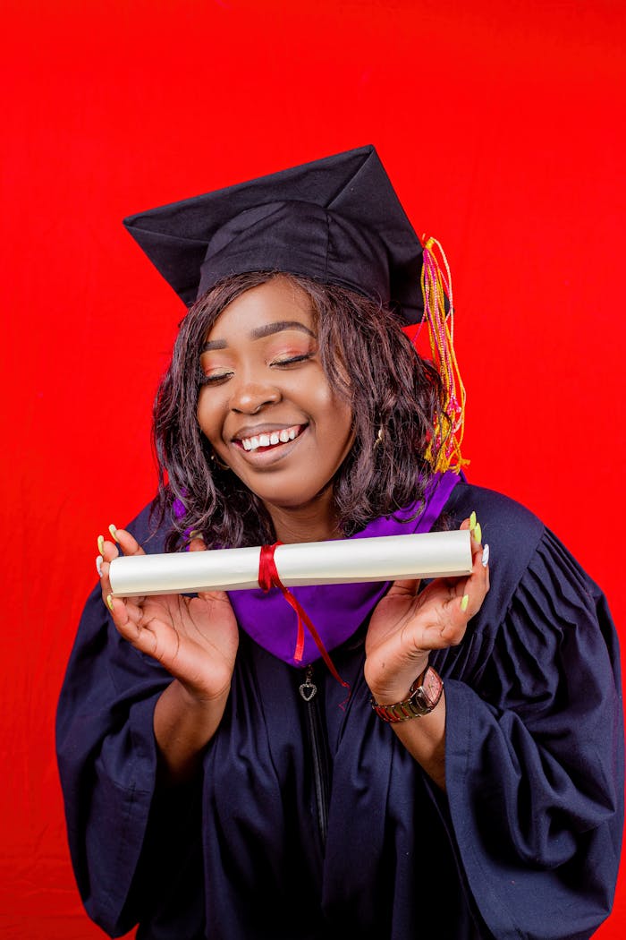 Happy graduate in cap and gown holding diploma against red background.